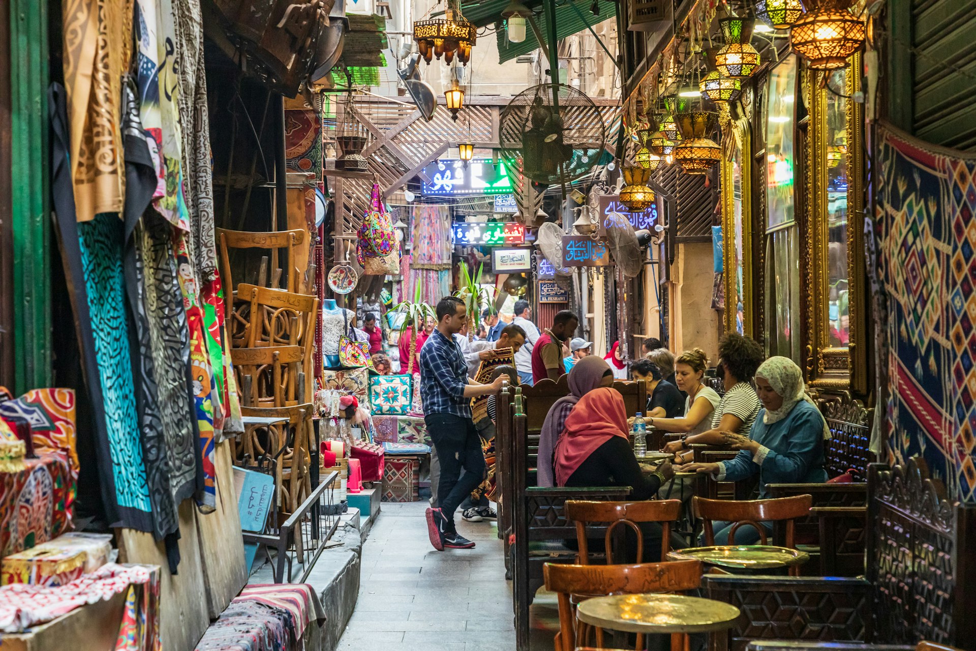 People sit at tables outside a coffee shop in a busy souk